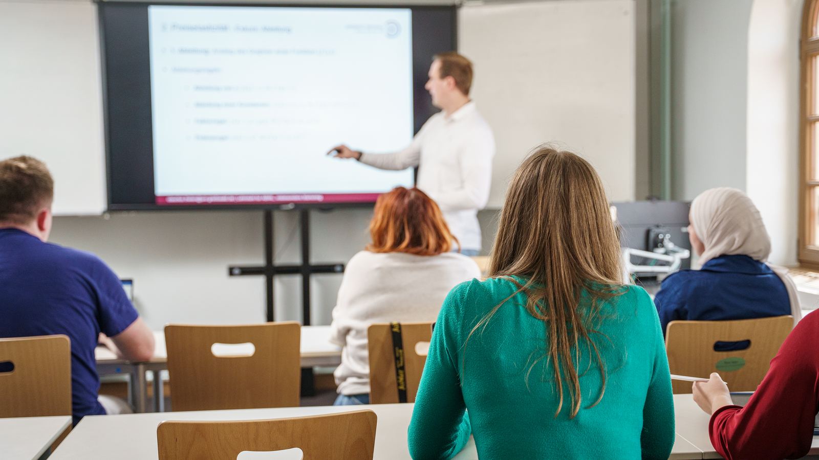 Übung im Seminarraum: Studierende von hinten, vorn erklärt Claudius Thelen eine Folie zur Preiselastizität