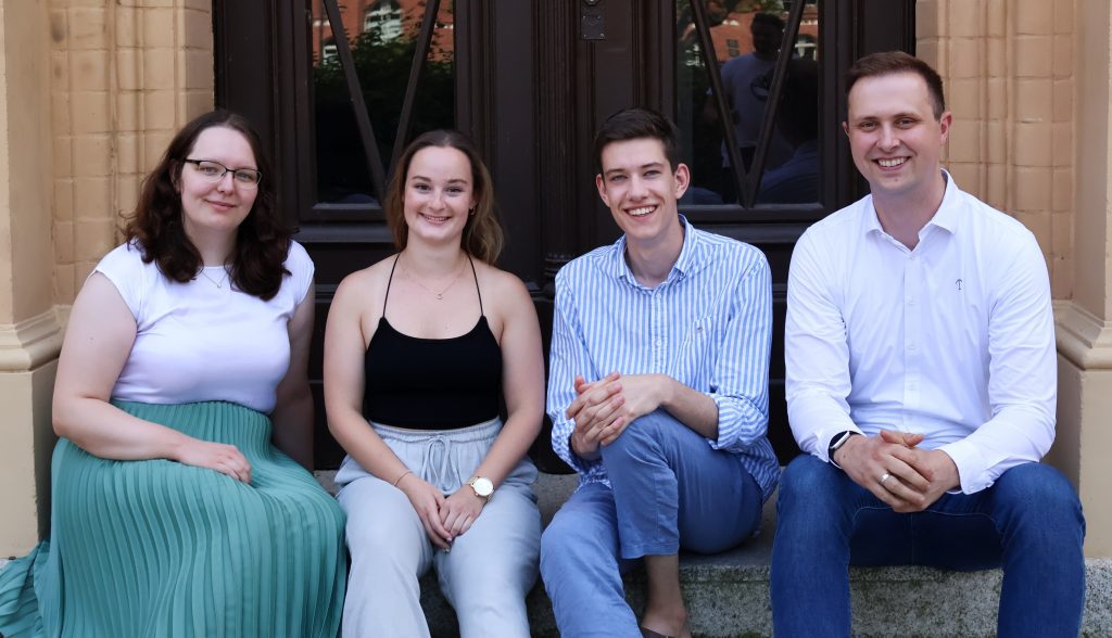 Vier Personen des Projektteams sitzen nebeneinander auf einer Treppe